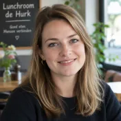 Lachende vrouw met halflang bruin haar en gouden oorring voor een krijtbord in een lunchroom